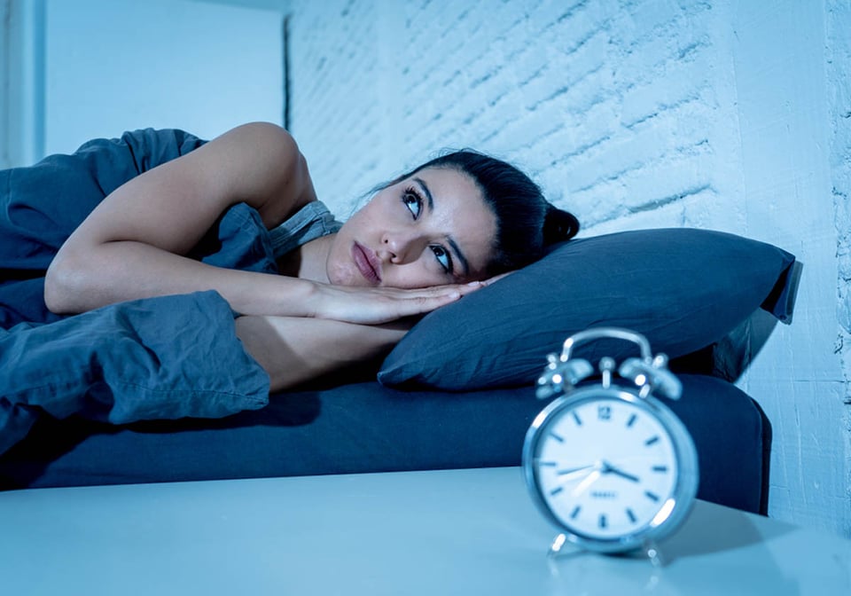 mujer hispana acostada en la cama, tratando de dormir, despertador, insomnio