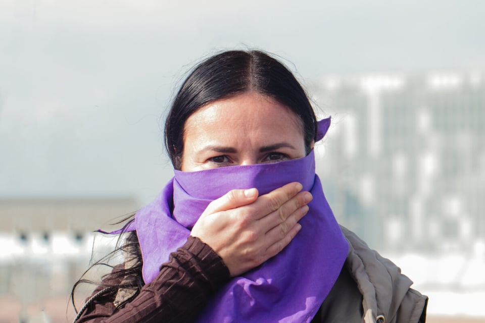 A woman with a purple scarf on her face and with her hand on her mouth