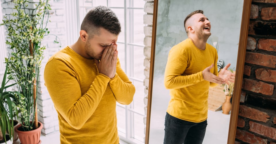 A man laughing at the other side of his mirror reflection