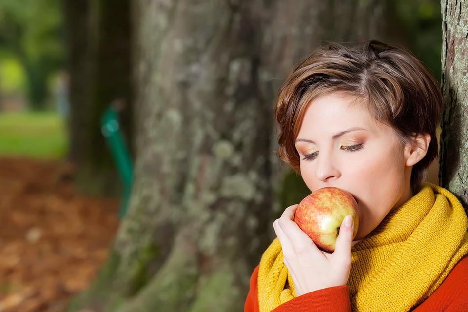 girl sitting against a tree, eating an apple, park